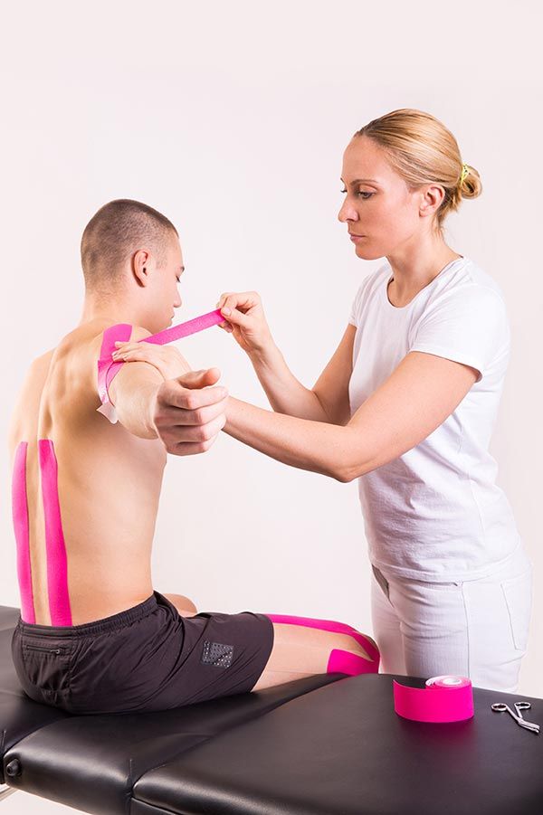 Physical therapist taping a seated patient’s back and shoulder on a treatment table