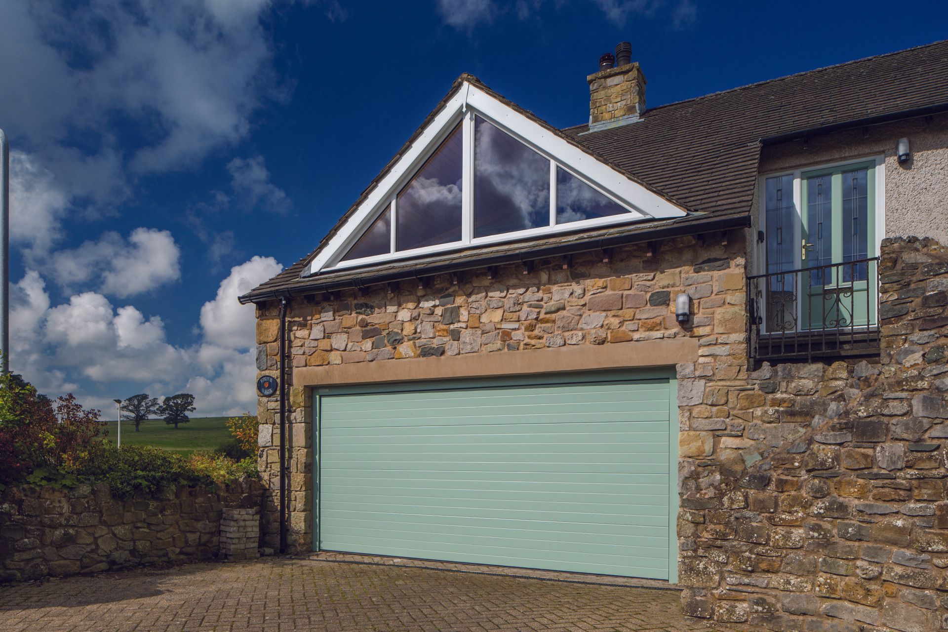 A newly fitted green garage door on a large brick house
