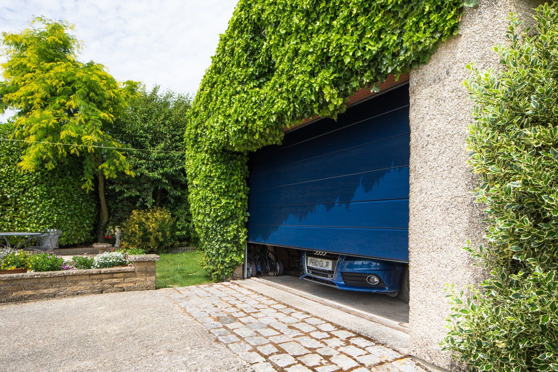 A newly fitted garage door covered in plants opening with a car exiting