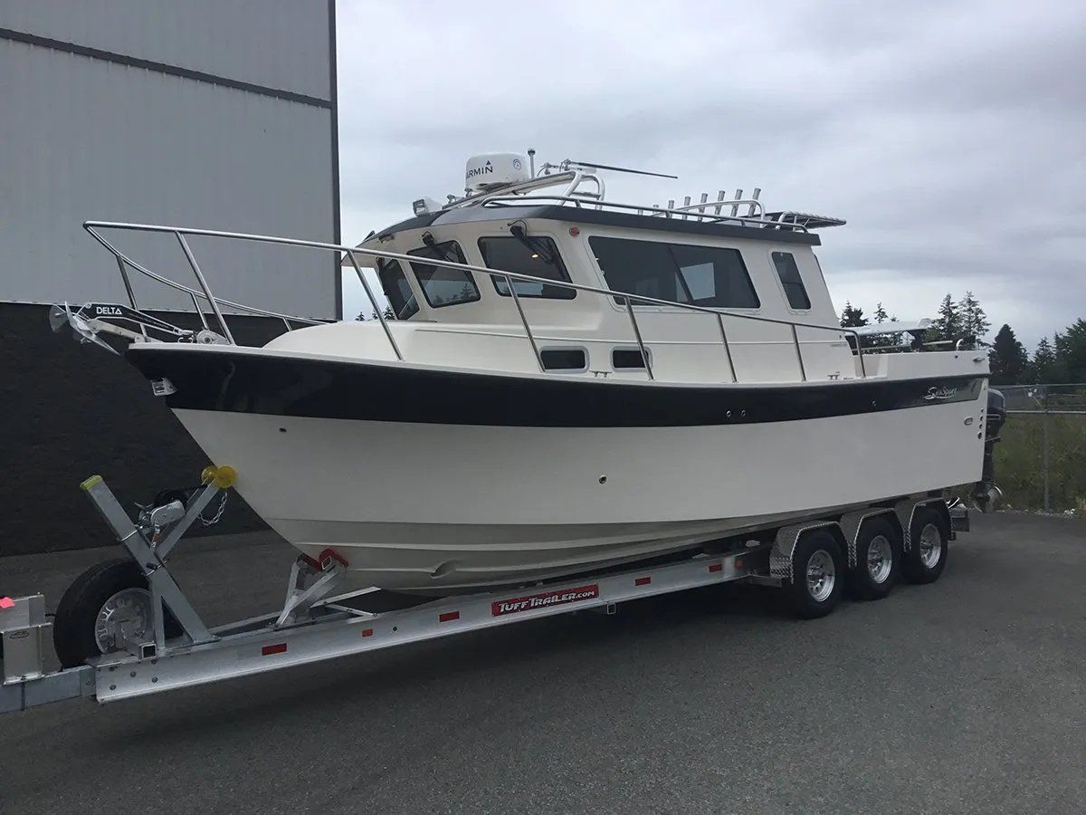 White and black cabin cruiser boat on a trailer, with fishing rod holders, against a cloudy sky.
