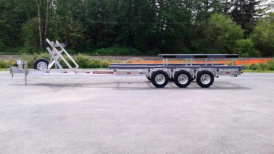 Aluminum boat trailer on a paved surface. Three sets of wheels, rollers, and a winch stand.