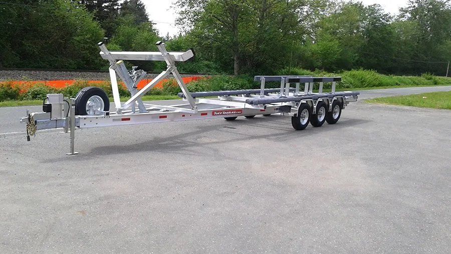 Aluminum boat trailer on asphalt with trees in the background.