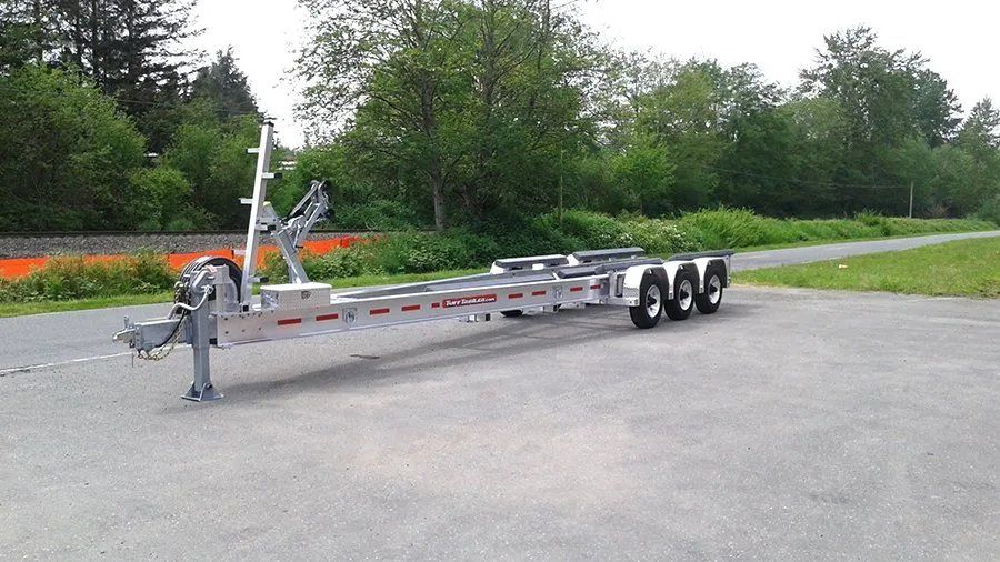 Aluminum boat trailer with three axles on a paved lot.