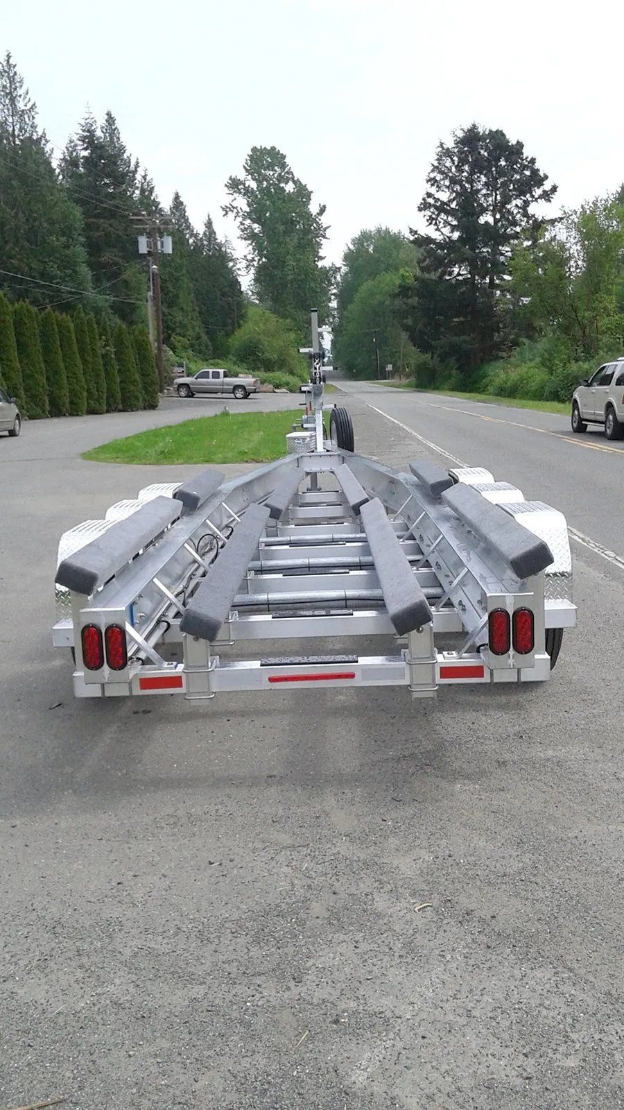 Boat trailer on a paved road, viewed from the rear. Silver frame, black bunks, red taillights, parked outside.