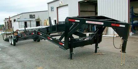 Black gooseneck trailer with red and white reflective tape. It is parked outside a building.