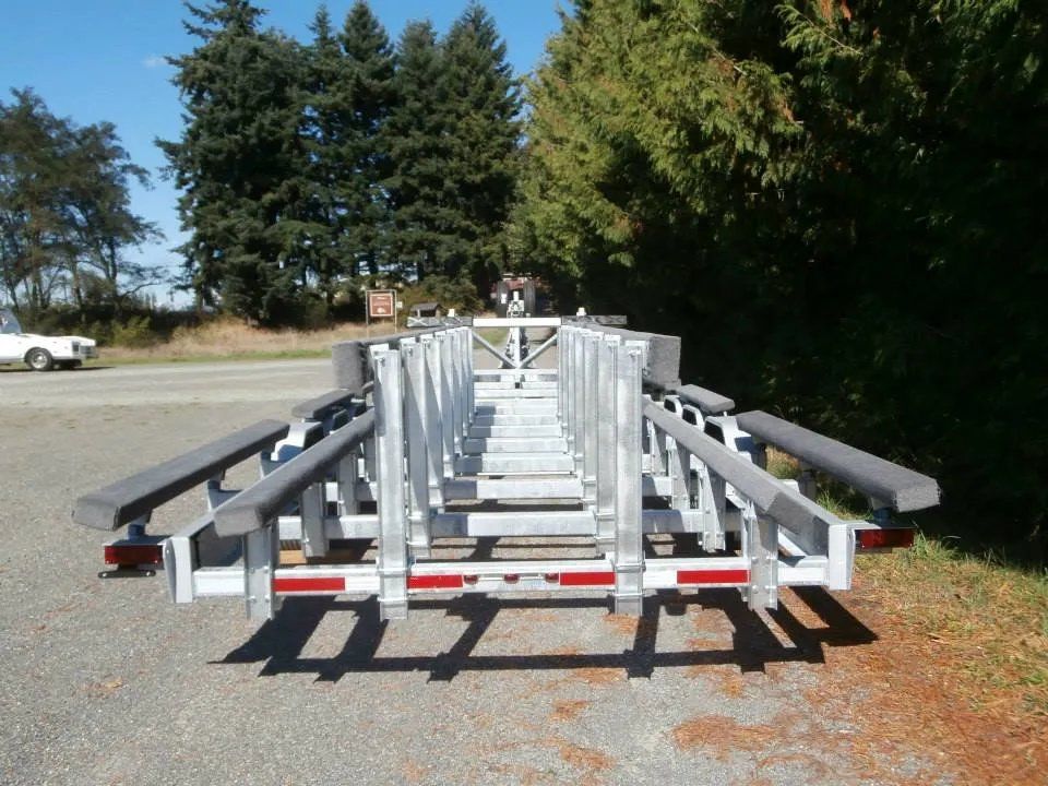 Boat trailer on gravel, with gray padded supports. Tail lights and a blue sky are visible.