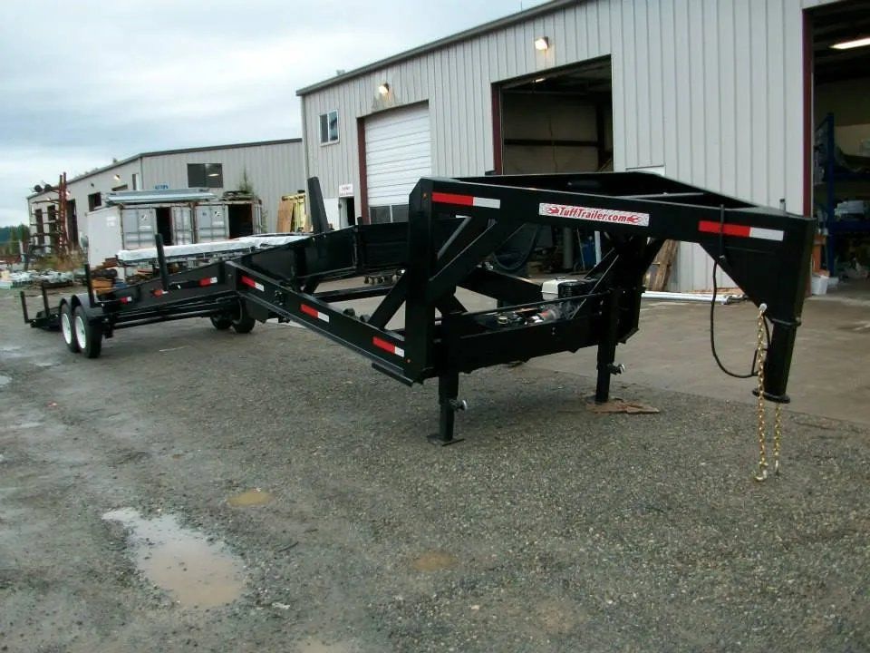 Black gooseneck trailer with red and white reflective tape, parked on gravel. Buildings in the background.