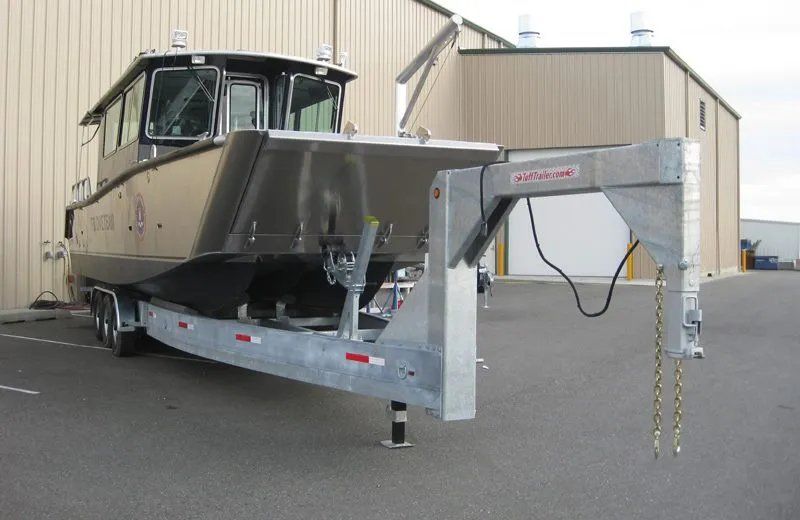 Boat on a silver gooseneck trailer, parked in front of a metal building.