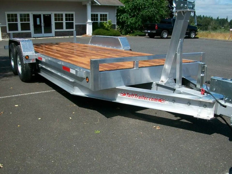 Aluminum car trailer with wooden deck in a parking lot.