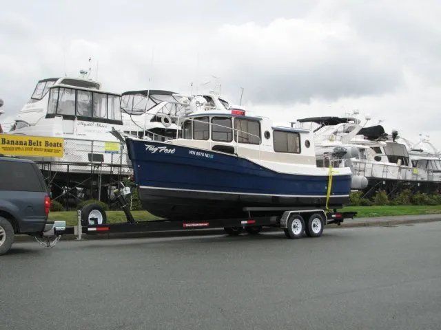 Blue and white boat on a trailer parked next to other boats on land under a cloudy sky.
