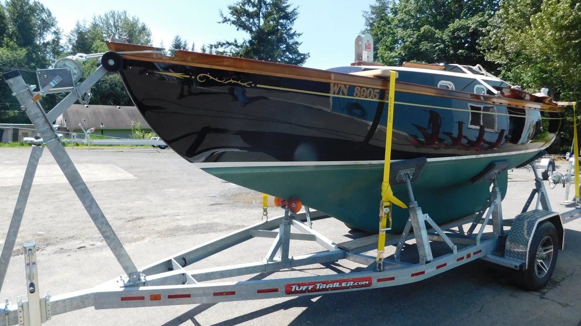 Black and green sailboat on a trailer, outside, with wooden trim.