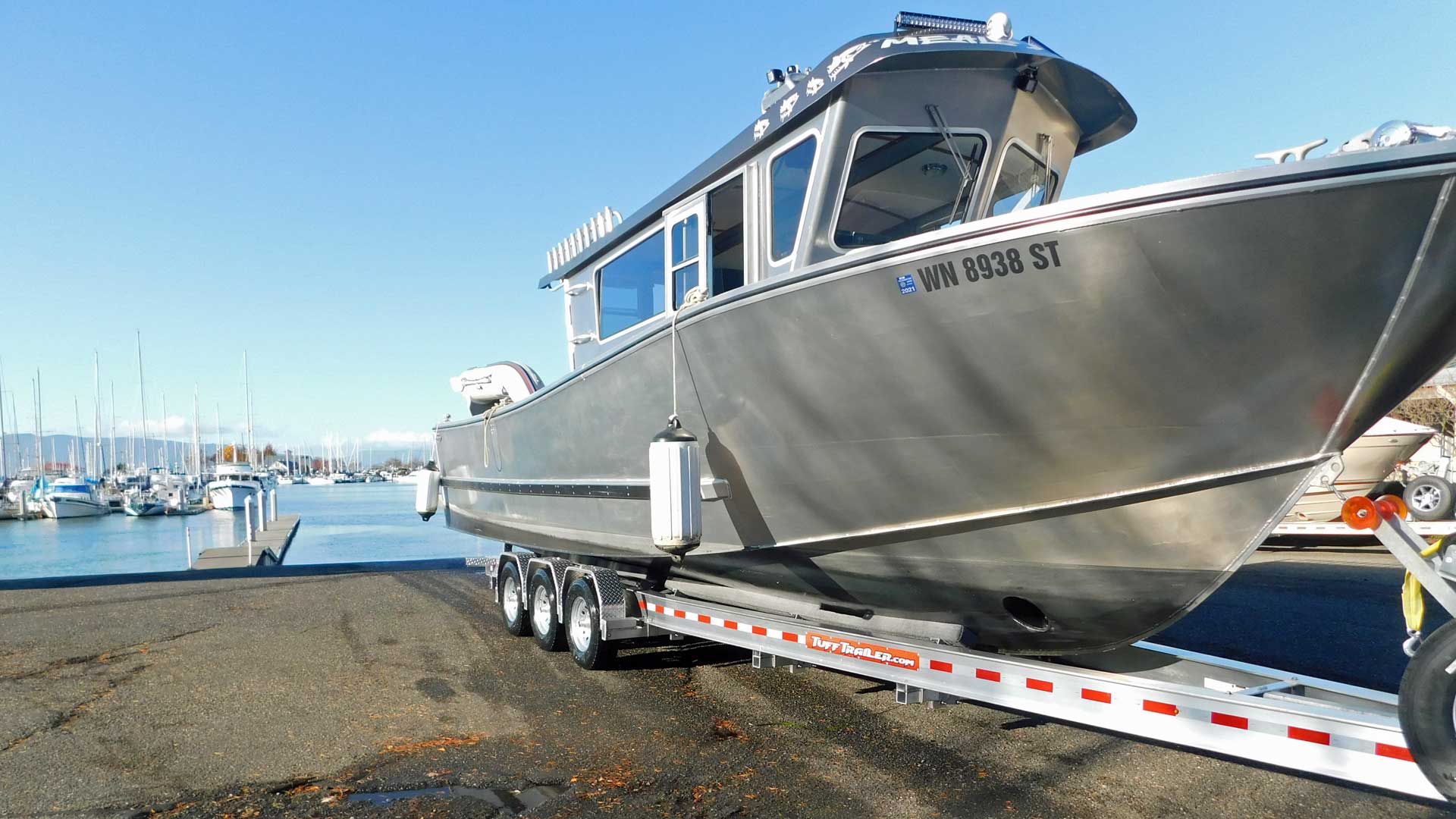 Gray aluminum boat on trailer at a dock, clear sky.