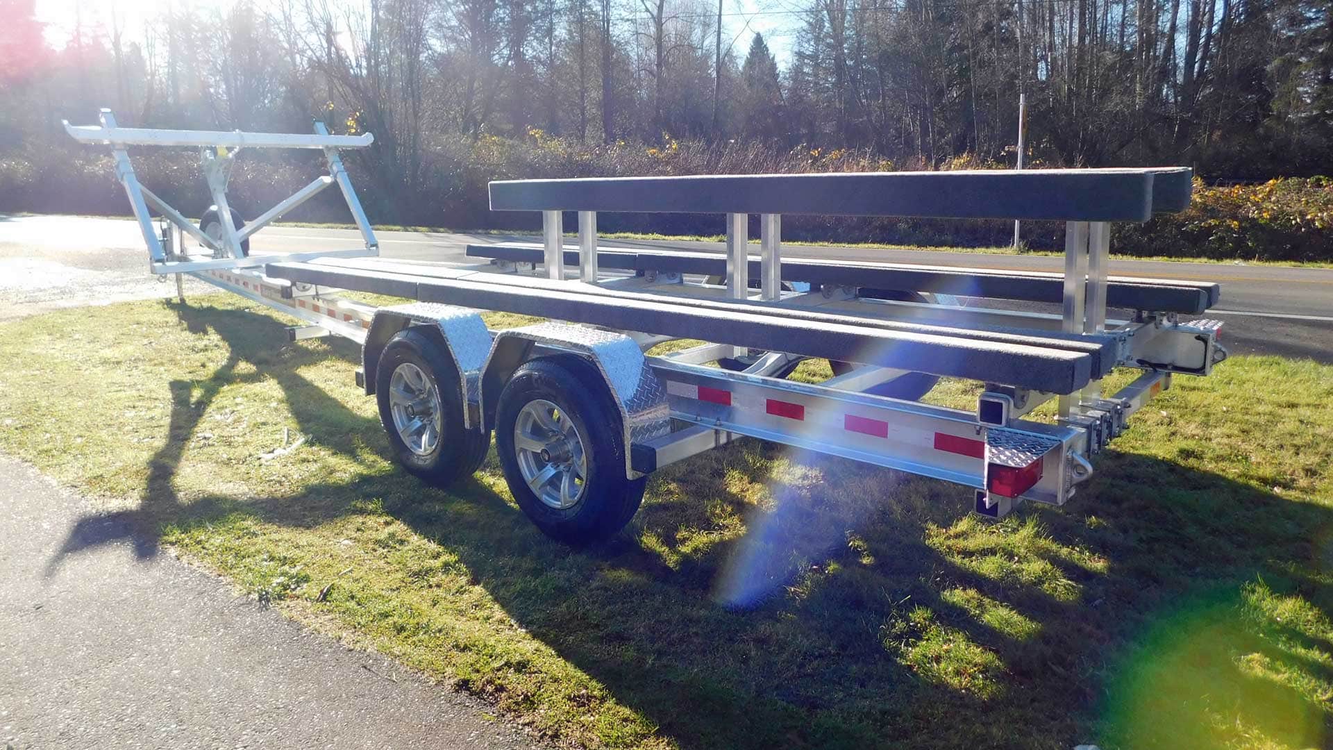 Boat trailer on grass with two axles, supports, and a hitch.