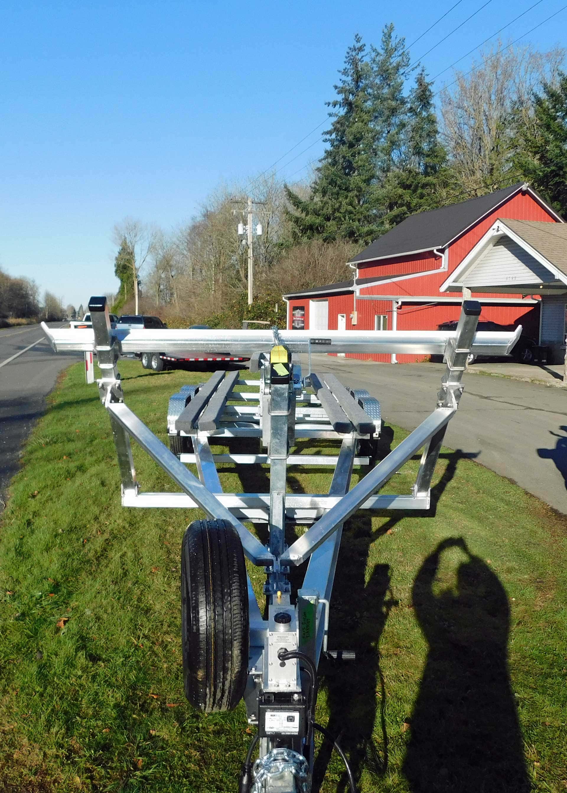 Boat trailer parked on grass, with a road and red building in the background.