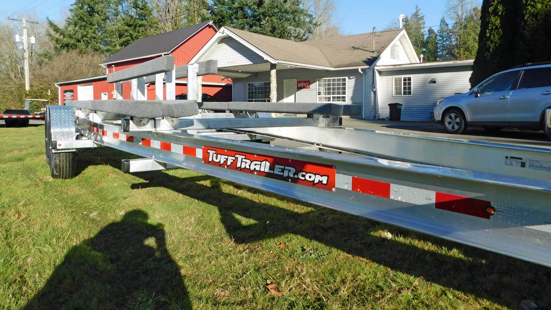 Silver boat trailer parked on grass in front of a house.