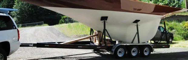 A sailboat on a trailer being towed by a white SUV. A black truck is parked in the background.
