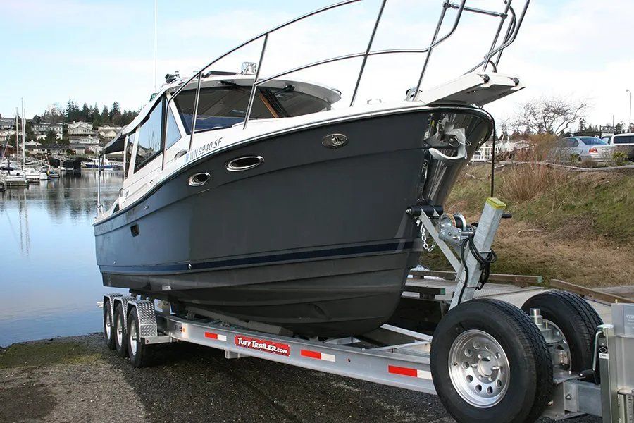 Boat on a trailer at a boat ramp; blue hull, white cabin, chrome accents, gray sky.