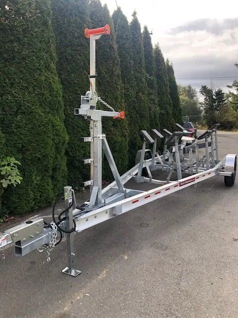 Silver boat trailer with a tall, red-topped pole, parked on pavement, with evergreen trees in the background.