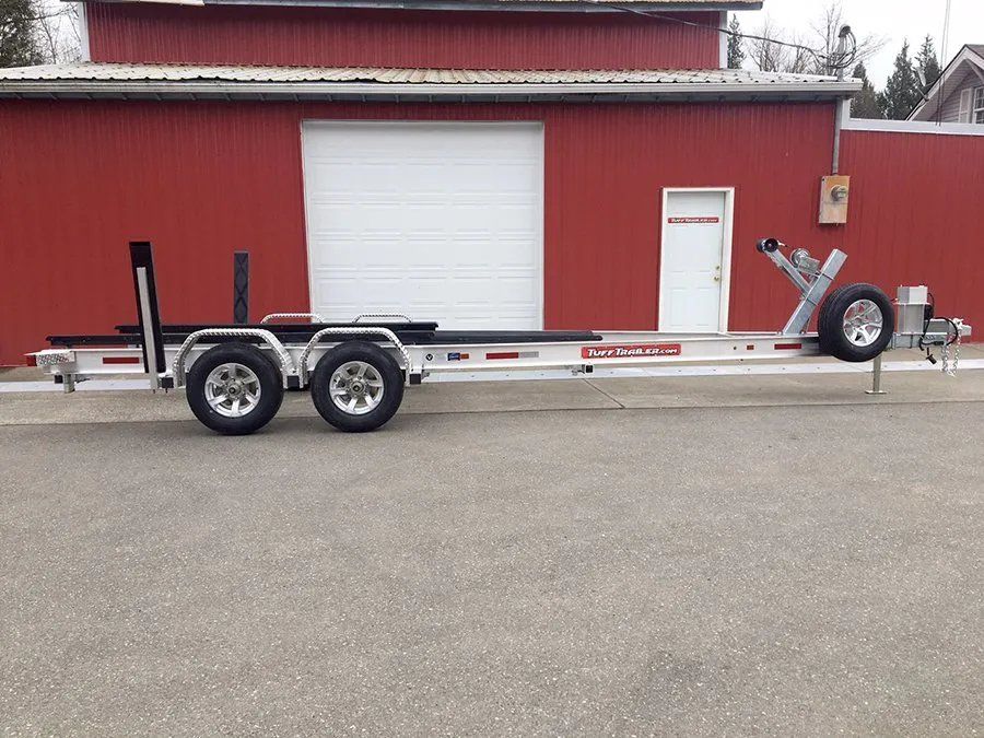 A white boat trailer with two axles parked in front of a red building.