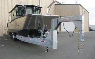 Gray boat on a trailer, attached to a gooseneck hitch. Building in background.