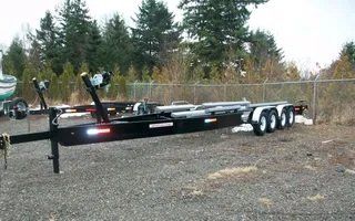 Black boat trailer with three axles parked on gravel.