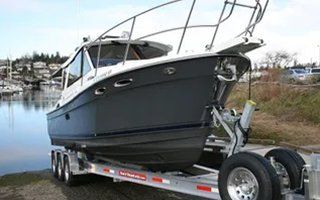 Boat on a trailer at a marina, with a dark blue hull and silver railings, parked near water.