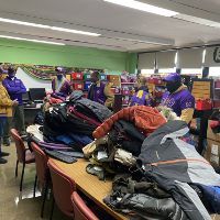A group of people are standing around a table with a pile of clothes on it.