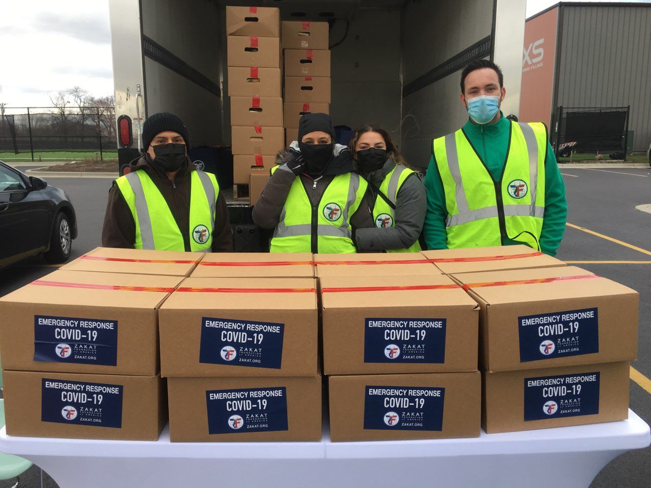 A group of people wearing masks are standing in front of a truck filled with boxes.