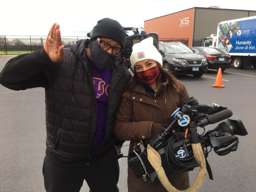 A man and a woman wearing masks are standing next to each other in a parking lot.