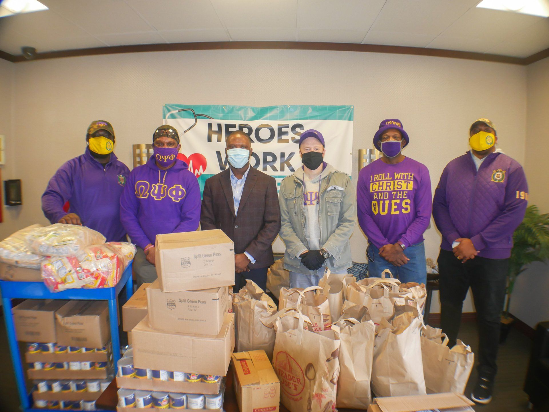 A group of men wearing masks are standing in front of a sign that says `` heroes work ''.