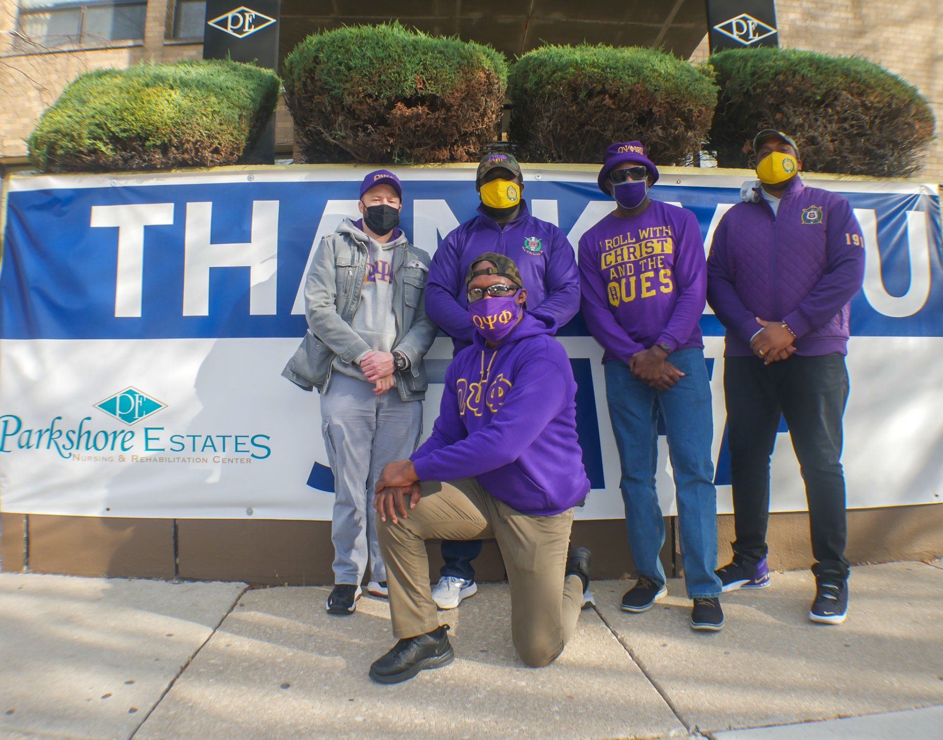 A group of men wearing masks pose in front of a thank you sign