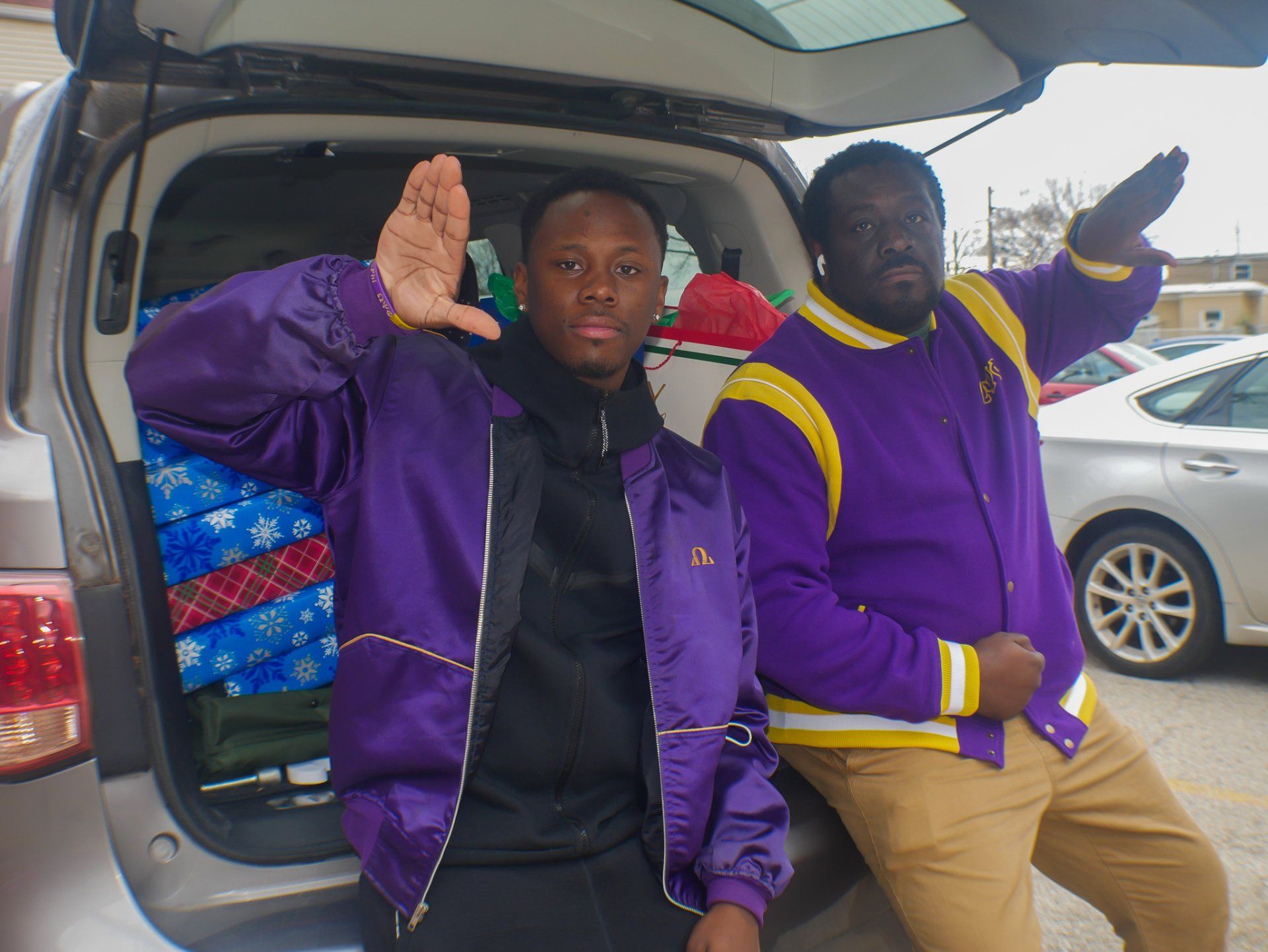 Two men in purple jackets are standing in the back of a car