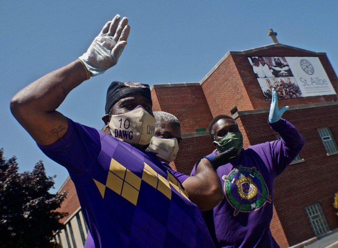 Two people wearing face masks and gloves are waving in front of a building
