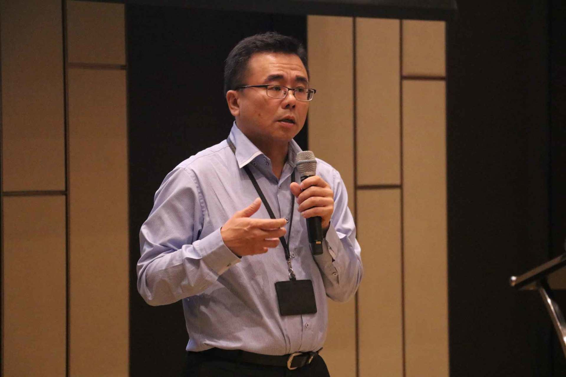 一名身穿淺藍色襯衫的男子在會議上對著麥克風講話。