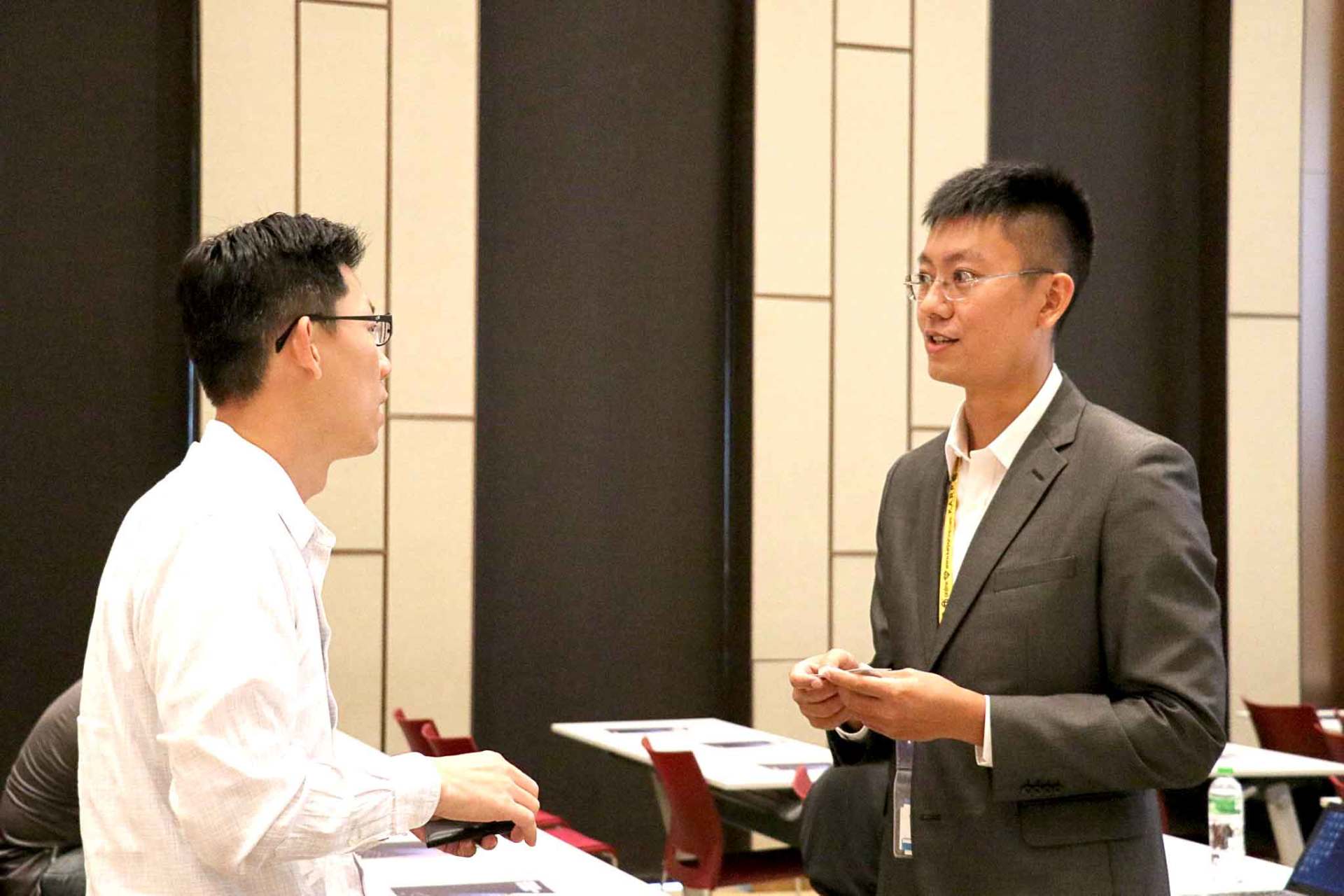 會議現場，兩名男子麵對面交談，其中一人穿著西裝。