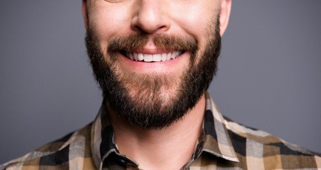 Smiling man with a full beard, wearing a plaid shirt against a gray backdrop.