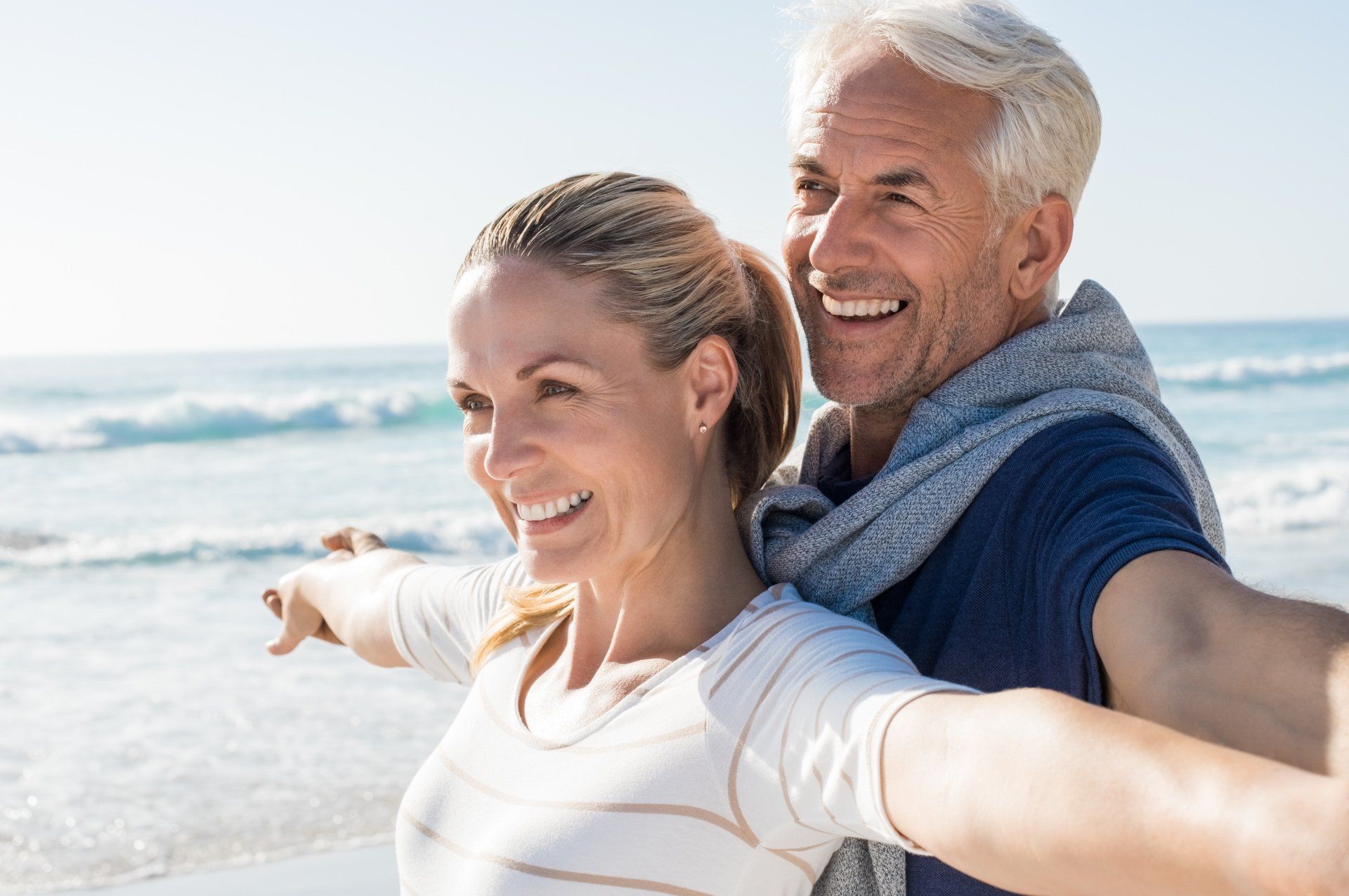 A man and a woman are standing on the beach with their arms outstretched.