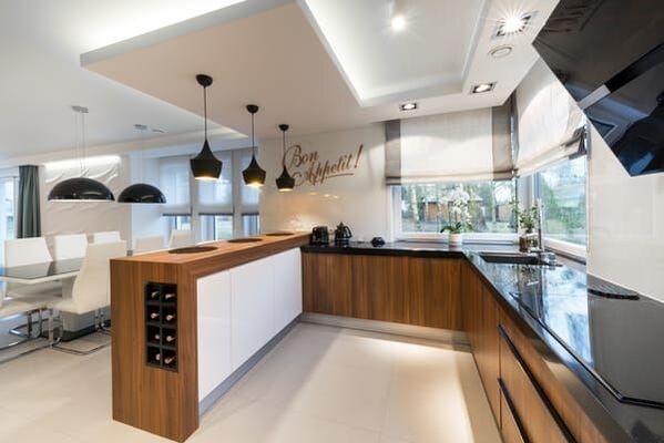 Roman blinds on windows of timber kitchen, with black benchtops, and black stylish pendant lights.