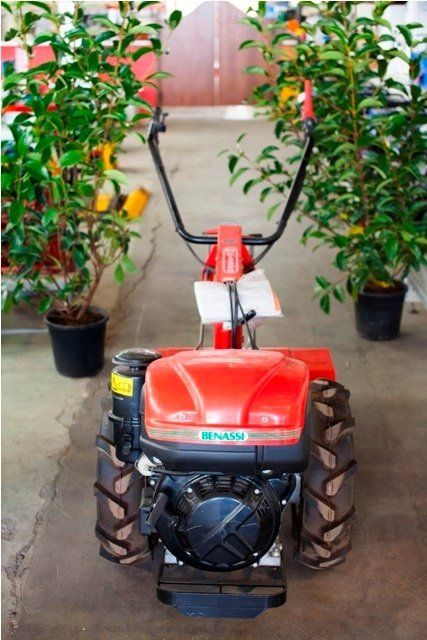 Motocoltivatore rosso con manici neri, posizionato tra piante in vaso, in casa.