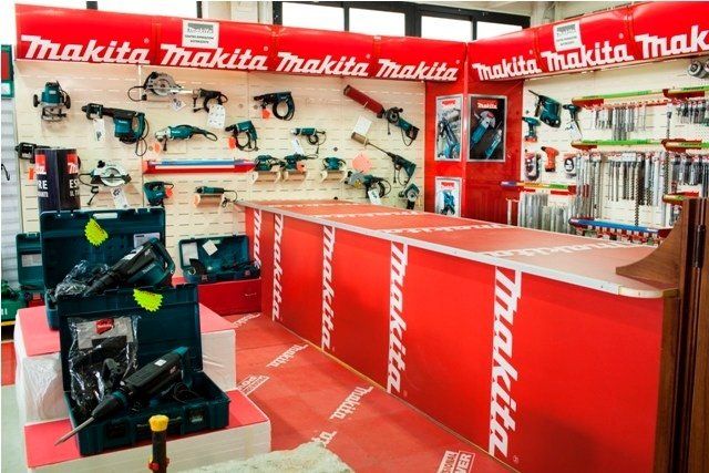 Un espositore di utensili Makita in un negozio, con vari utensili elettrici, marchio rosso e bianco e bancone espositivo.