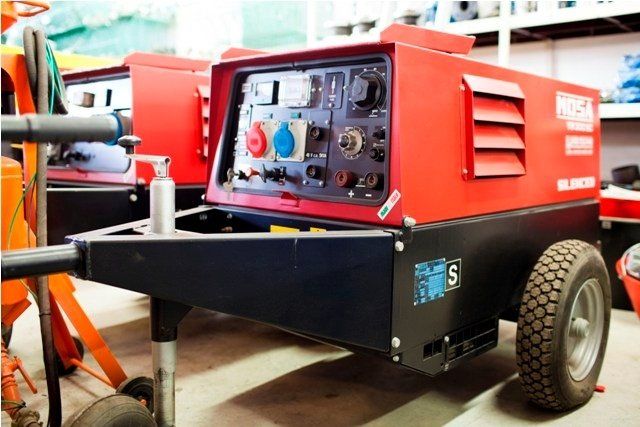 Generatore di saldatura rosso e nero su un rimorchio con prese elettriche.