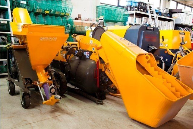Attrezzatura da costruzione gialla in un magazzino, tra cui tramoggia e macchinari.