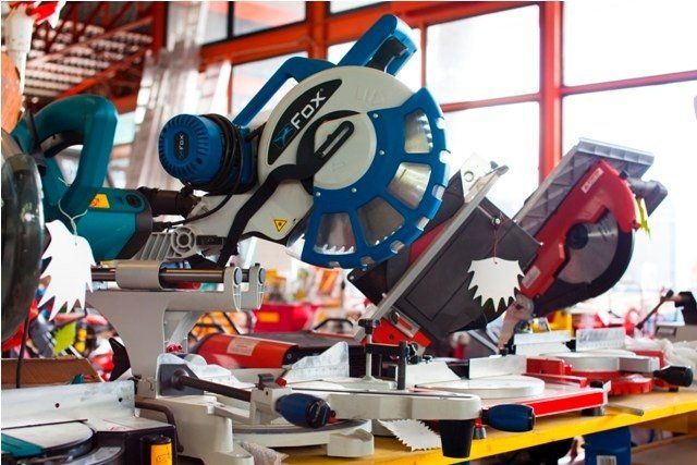 Pila di varie seghe elettriche su un tavolo giallo in un'officina, tra cui anche delle seghe troncatrici.