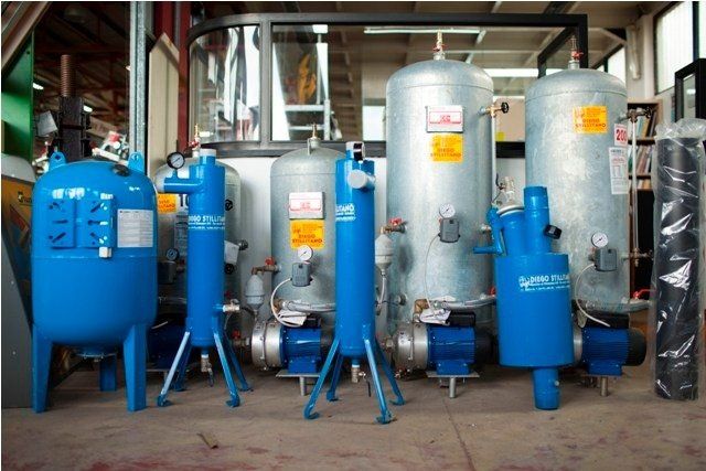 Attrezzature industriali blu e argento allineate in un magazzino, probabilmente per sistemi ad aria compressa.