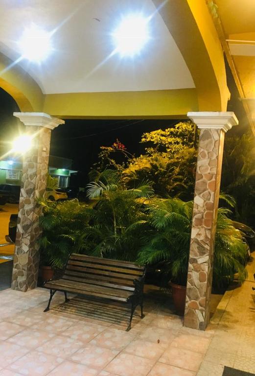 Zona de estar exterior cubierta con columnas de piedra, banco y plantas exuberantes por la noche.