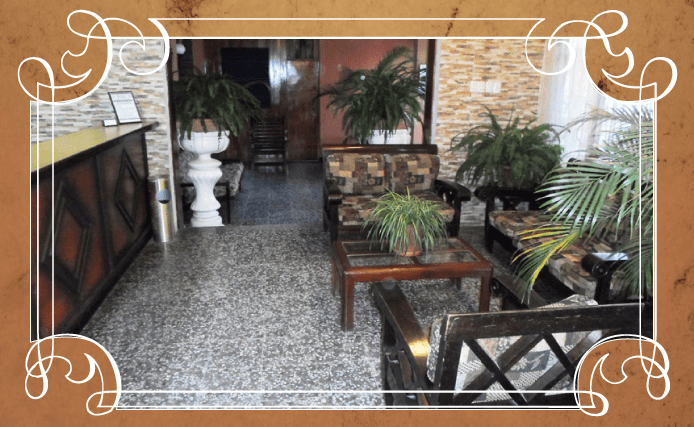 Patio interior decorativo con plantas en macetas, bancos de madera y muros de piedra bajo un borde ornamentado.