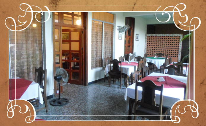 Comedor vacío de un restaurante con manteles blancos, servilletas rojas y sillas de madera.