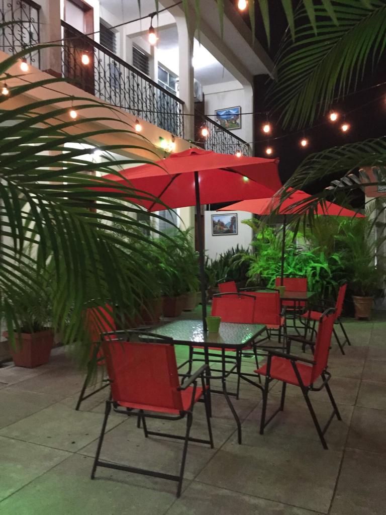 Patio exterior con mesas y sillas rojas bajo guirnaldas de luces y una sombrilla roja.