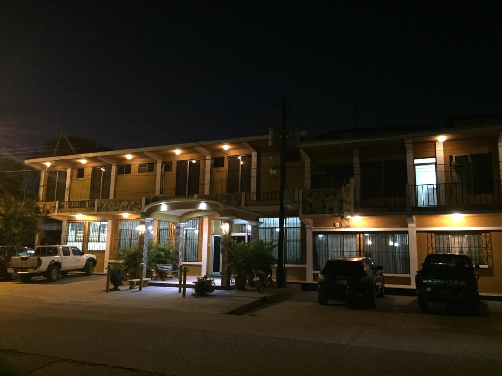 Vista nocturna de un motel de dos plantas con balcones iluminados, coches aparcados y una entrada cubierta.