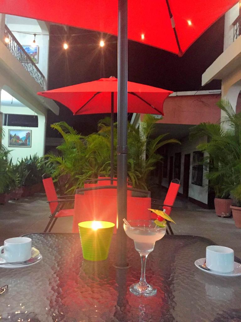 Terraza de una cafetería al aire libre con sombrillas rojas, una vela encendida, una copa de cóctel y vasos blancos 